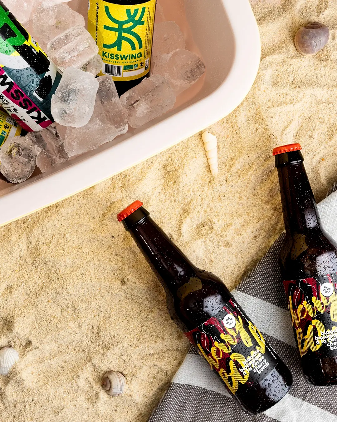 Lifestyle bières artisanales Kisswing : glacière, glaçons, sable, coquillages, serviette, été