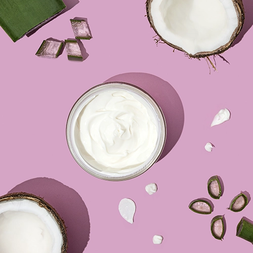 Crème cosmétique coco : pot ouvert, noix de coco et aloe, texture onctueuse, fond rose pastel