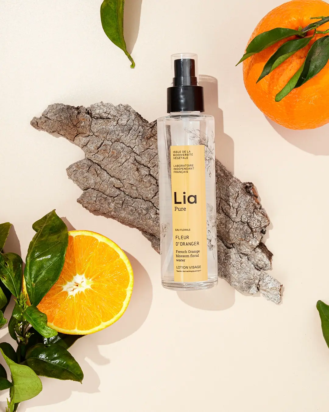 Spray Lia Pure Fleur d'Oranger, oranges fraîches, feuilles, bois naturel, fond beige lumineux