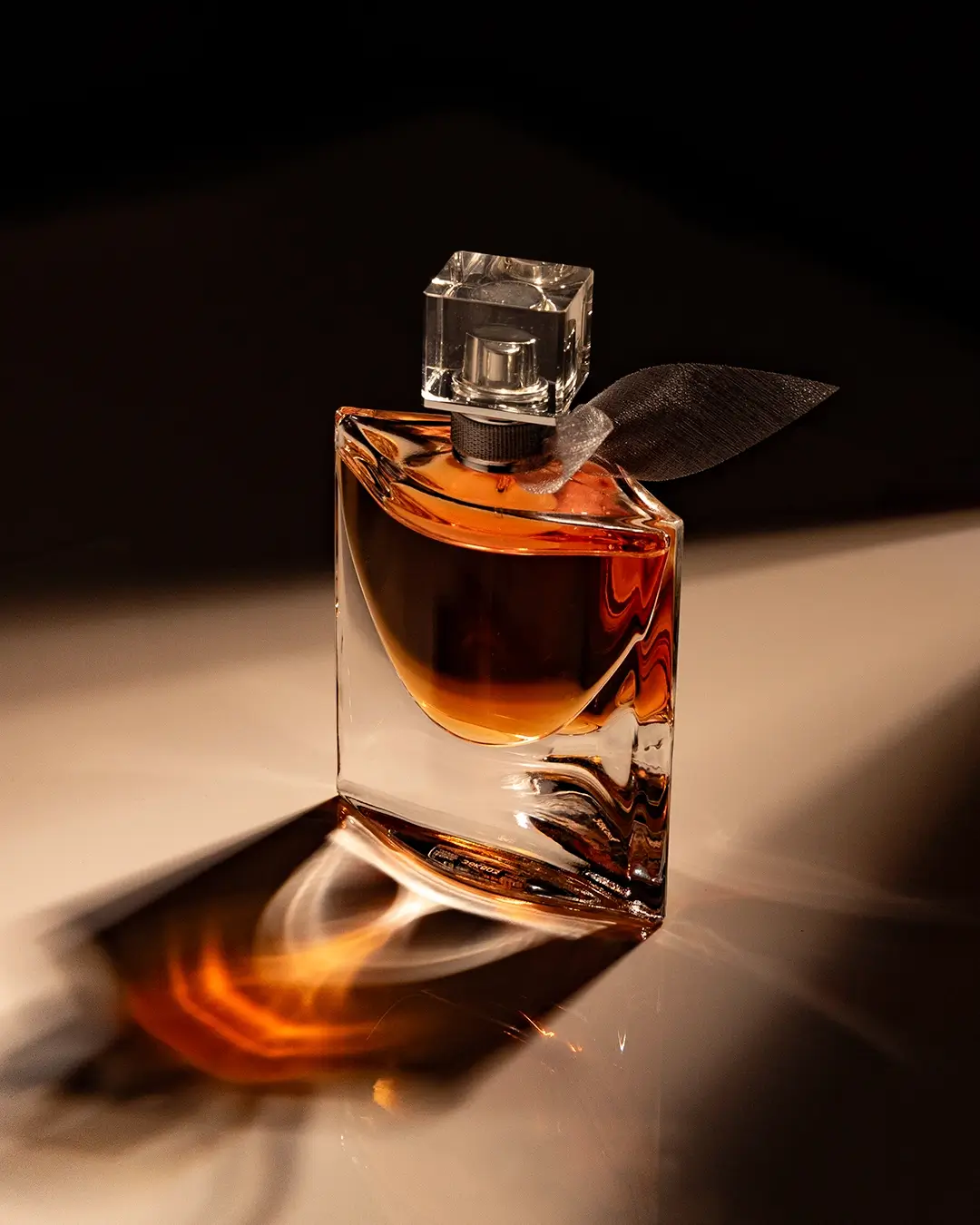 Flacon de parfum luxueux, bouchon carré transparent, verre épais, lumière dorée, reflet artistique