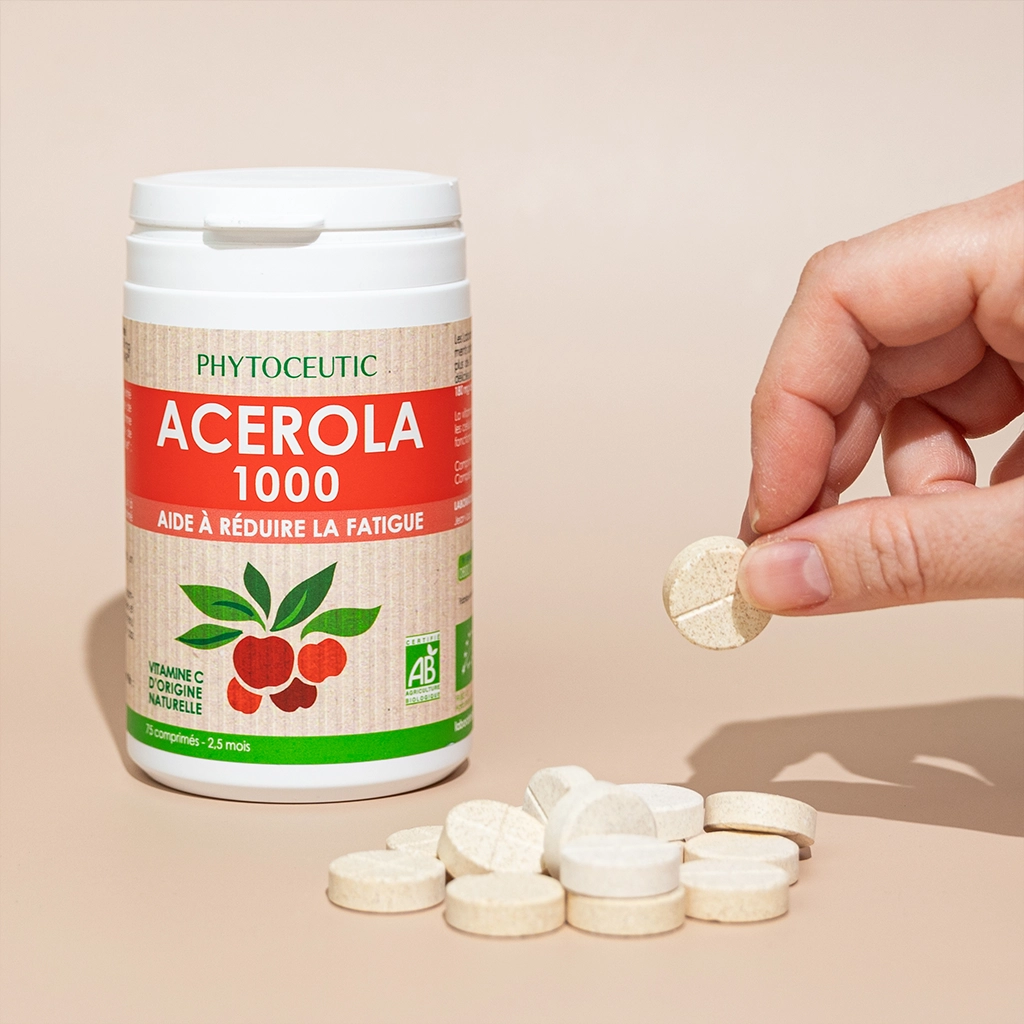 Complément Acérola 1000 Phytoceutic, main tenant comprimé, pile de comprimés sur fond beige.