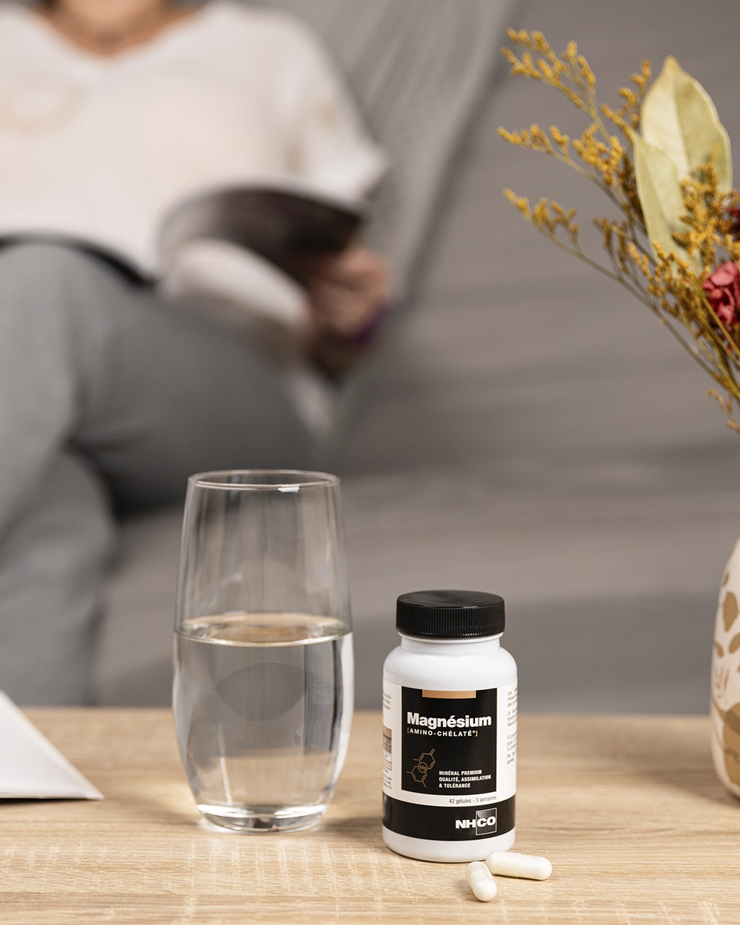 Photo lifestyle : pilulier magnésium, verre d’eau, fleurs séchées, ambiance bien-être, capsule NHCO