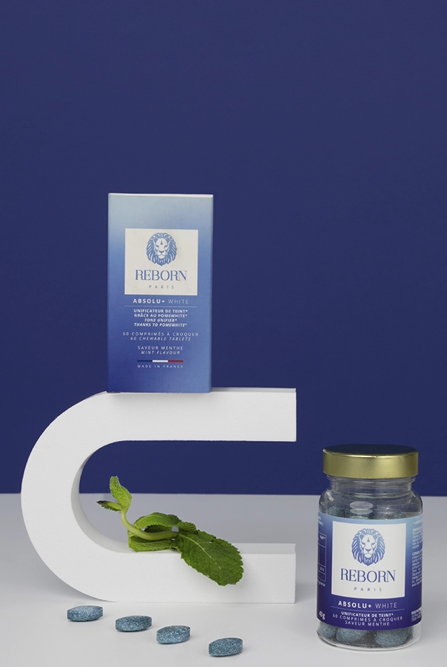 Comprimés Reborn Absolu+ White, boîte et pot bleu, podium blanc, menthe fraîche, fond bleu.