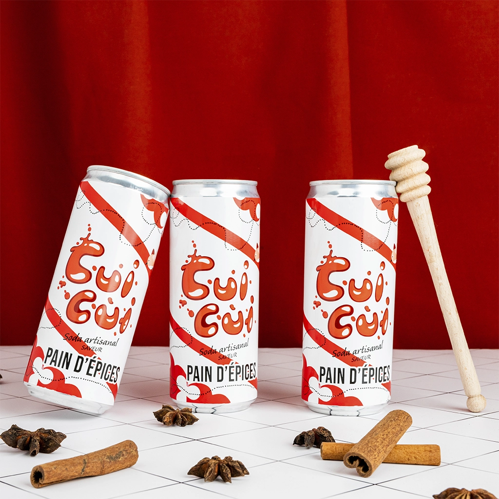 Trois canettes soda Cui Cui pain d'épices avec épices et cuillère à miel sur fond rouge.