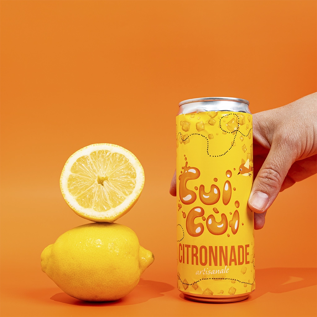 Main tenant canette citronnade Cui Cui avec citron frais sur fond orange vif.