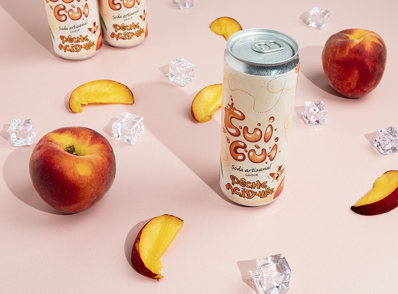 Soda Cui Cui pêche acidulée avec pêches fraîches et glaçons sur fond rose poudré.