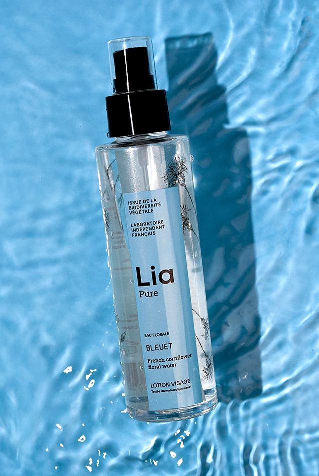 Lotion Lia Pure eau florale bleuet sur fond bleu aquatique avec reflets et gouttes.