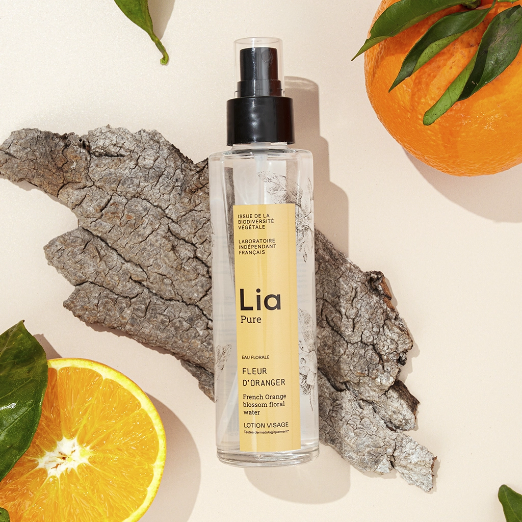 Lotion Lia Pure fleur d'oranger sur écorce avec orange fraîche et feuilles vertes.